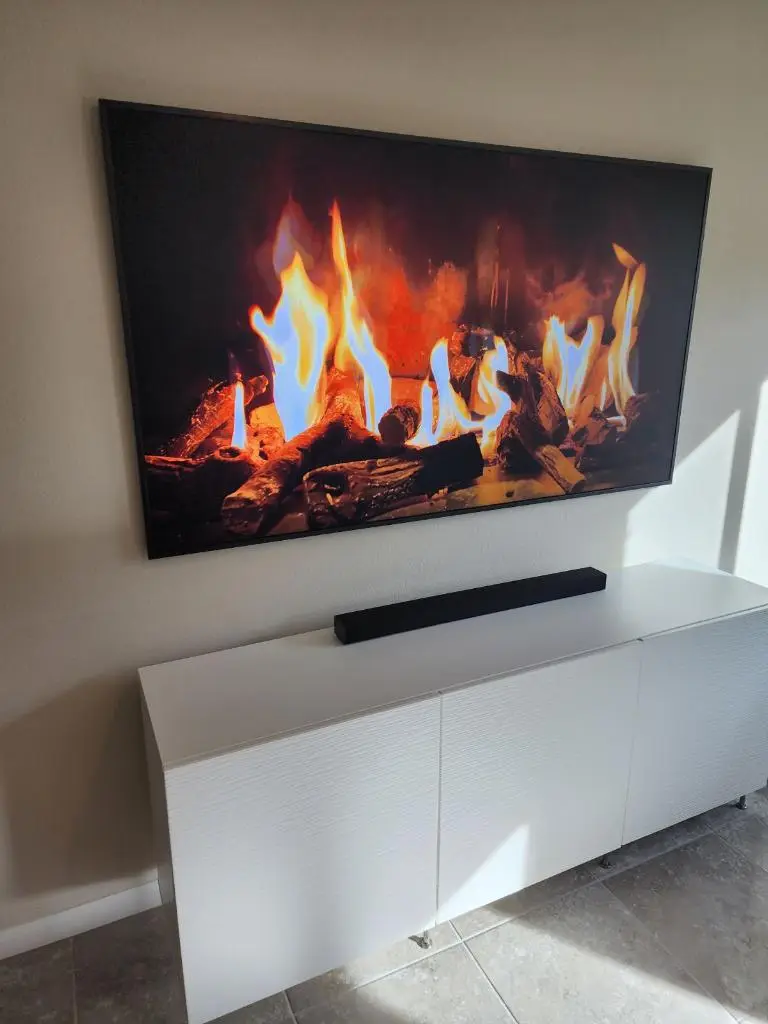 Large wall-mounted TV showing a fireplace scene above a white media cabinet and soundbar
